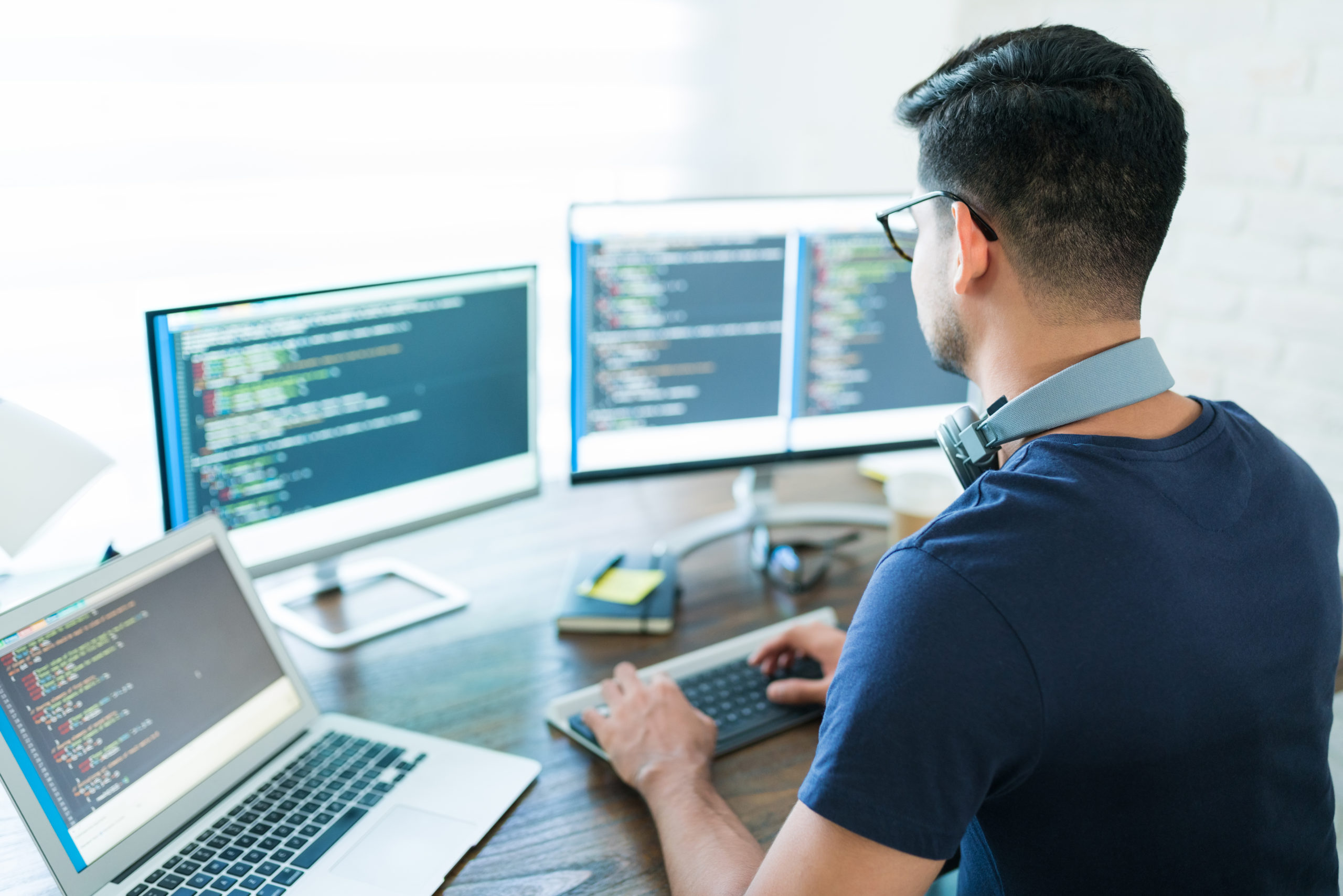 Rear view of man with dark hair working at a computer with three screens