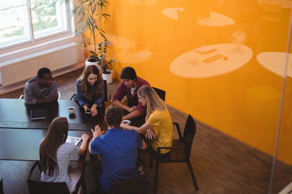 A group of people working together around a board room table in an orange room.